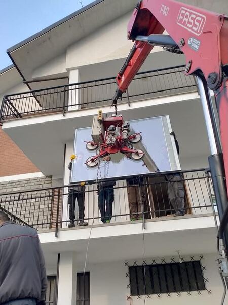 Sollevamento di vetrata tra balconi con gru FASSI in condominio